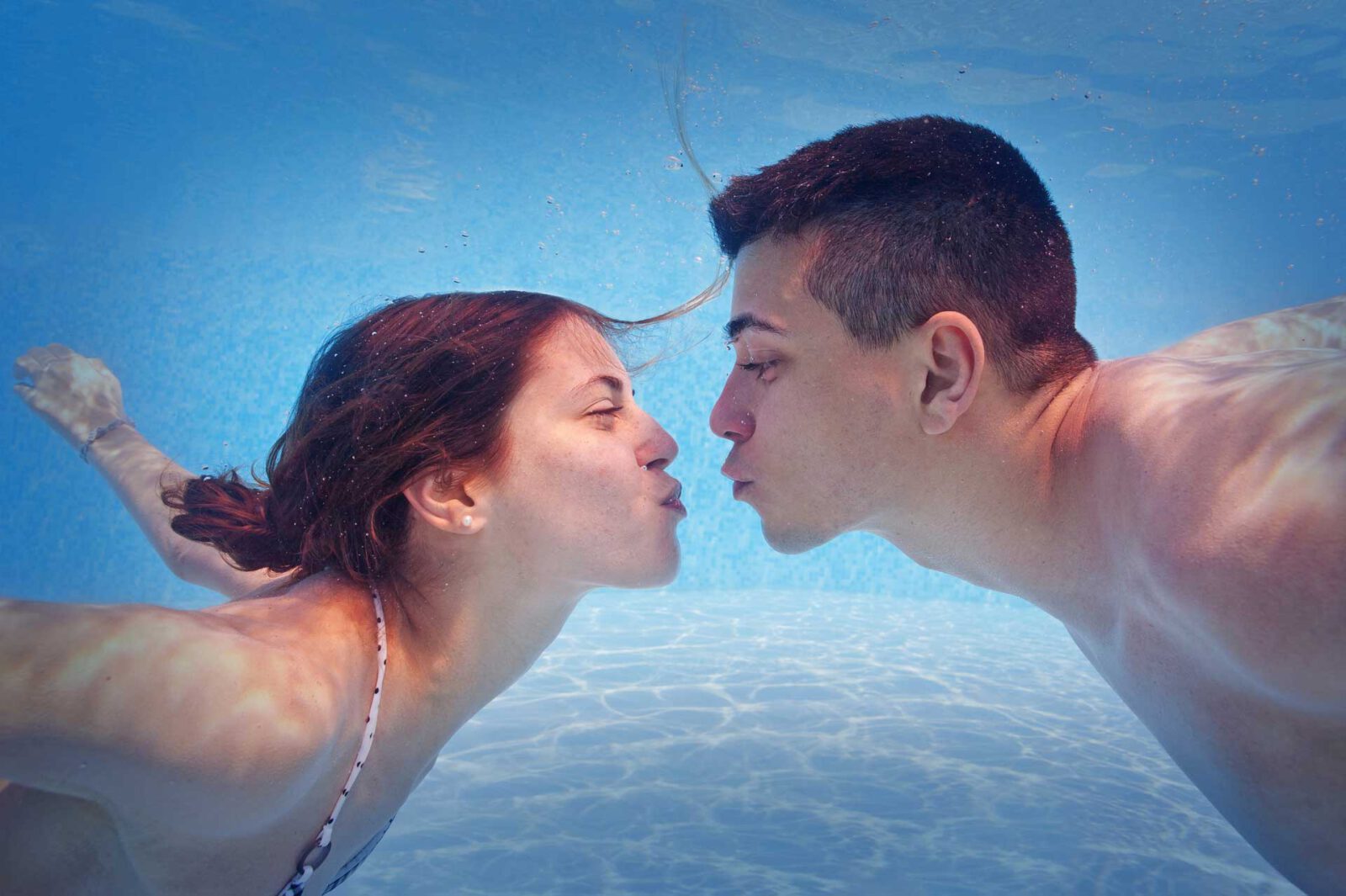 Ein junges Päarchen küsst sich im Schwimmbecken unter Wasser